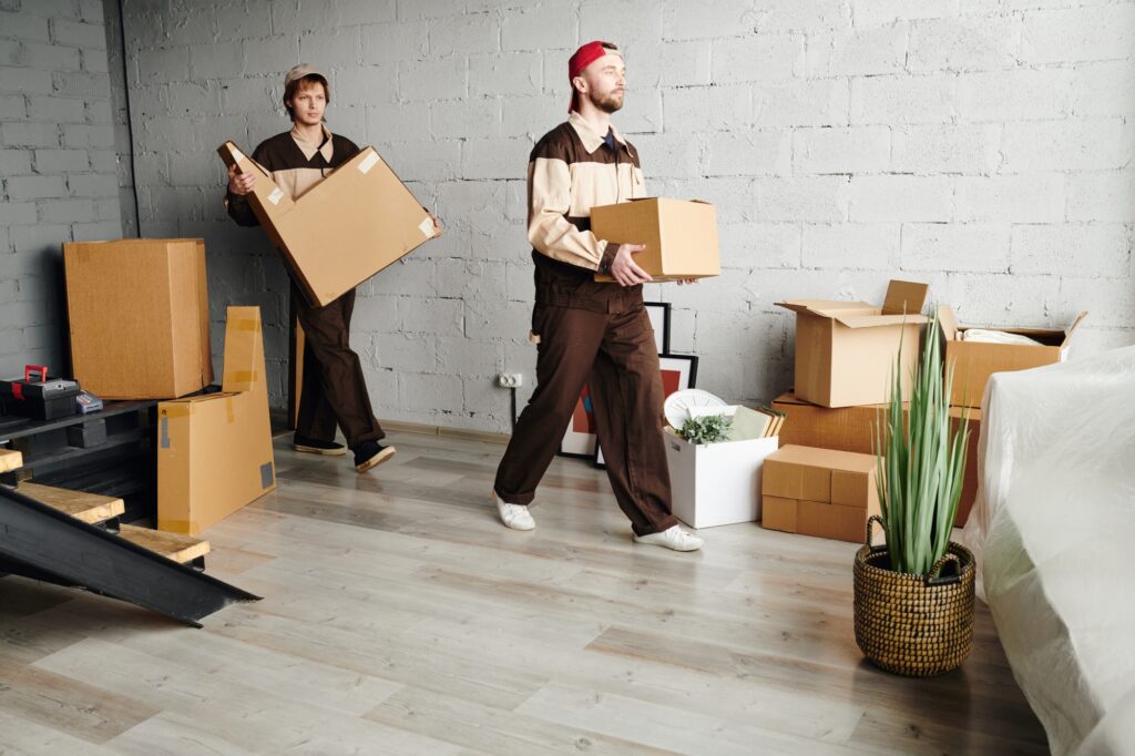 Two male movers carrying cardboard boxes from the house