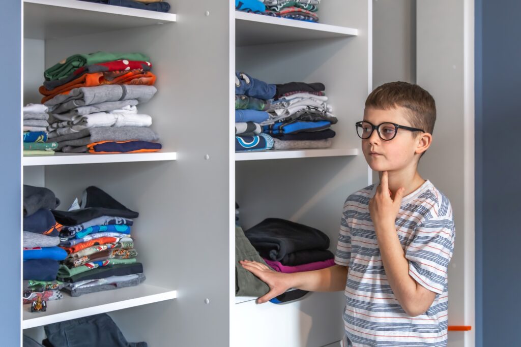 A young boy looks at his clothes in the closet in the concept of 'How to Pack Household Items Safely for a Move'.
