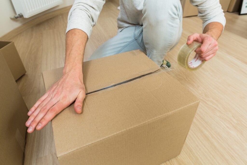 Closeup of a professional packer sealing a cardboard box with adhesive